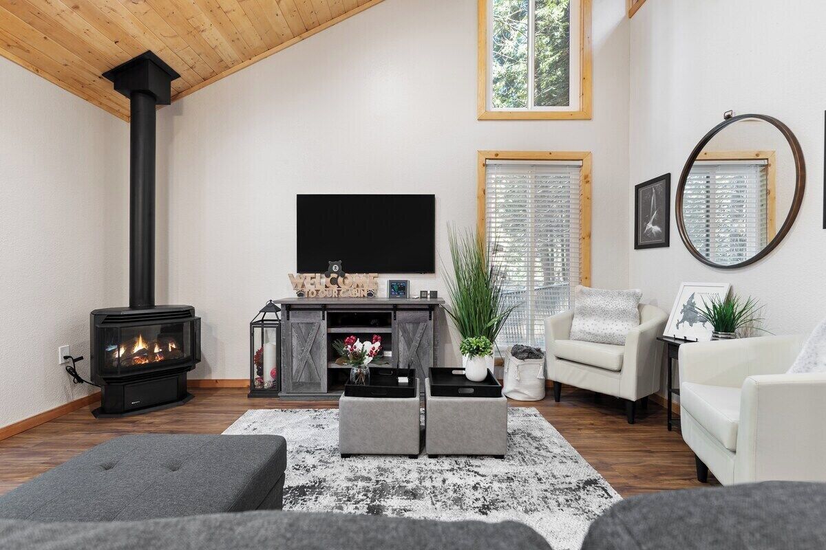 A cozy living room with a fireplace, a TV, comfortable seating, and a large window with blinds.