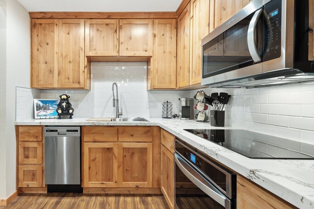 Een moderne keuken met houten kastjes, roestvrijstalen apparatuur en een witte betegelde achterwand.