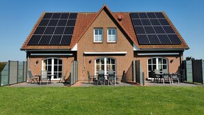 A two-story house with a brick facade, two solar panels on the roof, and a patio with outdoor furniture.