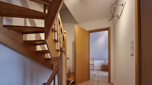 A wooden staircase leading to a room with a bed, a chair, and a nightstand.