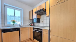 A kitchen with wooden cabinets, a dishwasher, a stove, and a window with flowers.