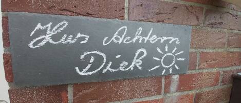 A chalkboard sign on a brick wall with the text "Mies Achtern Diek" and a sun symbol.