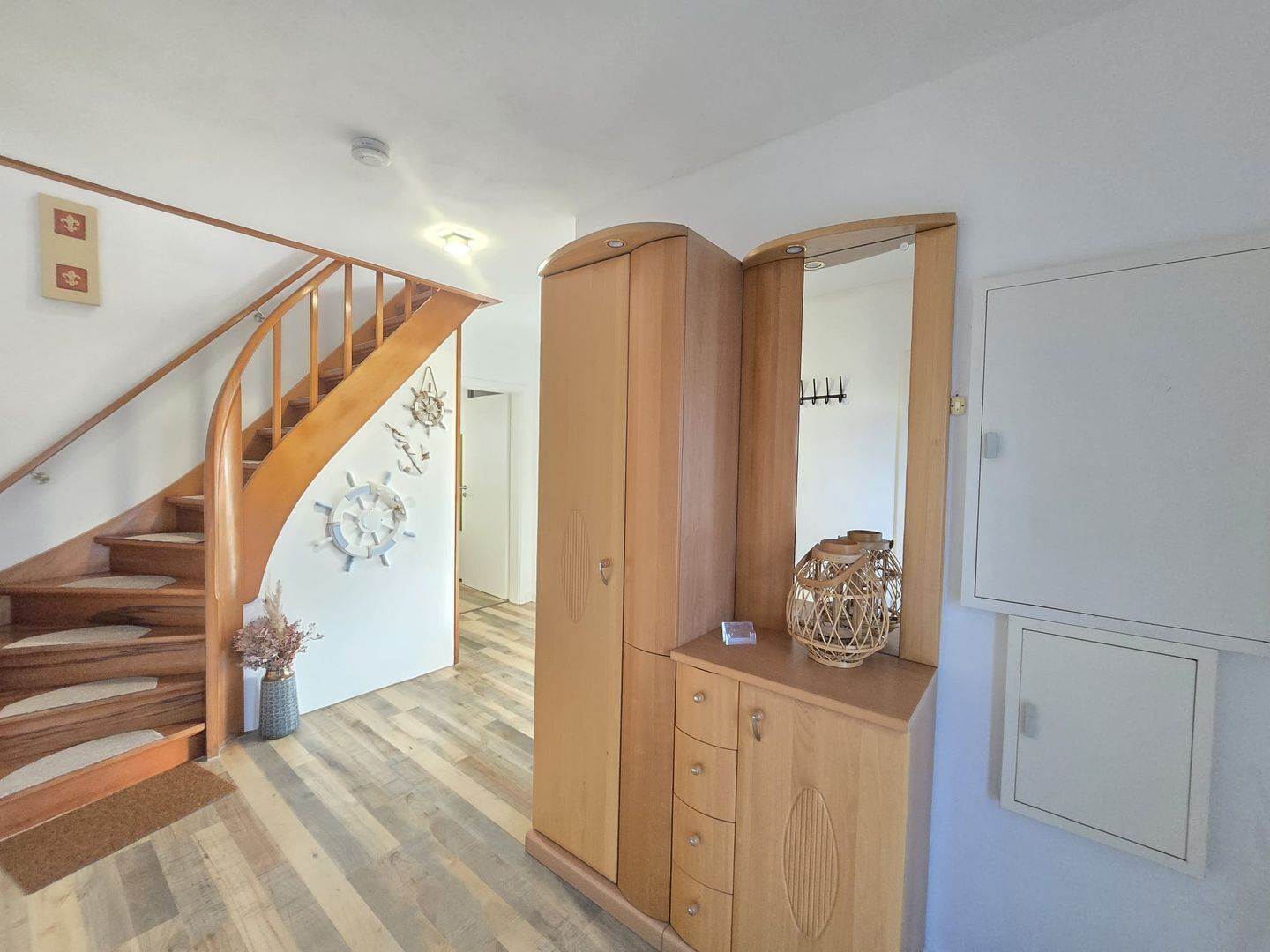 Eine Treppe mit Holzgeländern führt zu einer Zwischenebene, dort steht ein Holzschrank mit Spiegel und ein kleines dekoratives Objekt darauf.