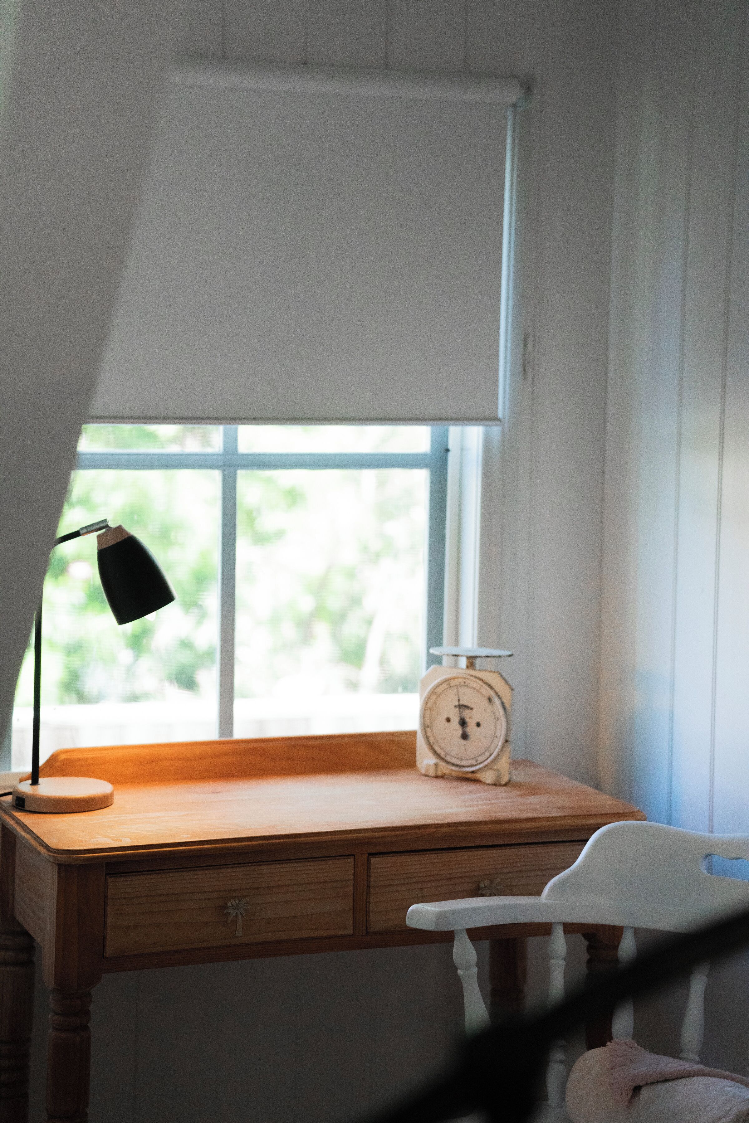 Un escritorio de madera con una lámpara, un reloj y una silla en una habitación con ventana.