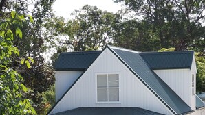 Une maison à deux étages avec un porche couvert, un panneau indiquant les places de stationnement réservées aux invités et des plantes en pot.