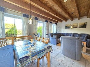 A cozy living room with a wooden ceiling, a dining table with a blue tablecloth, and a grey sofa.