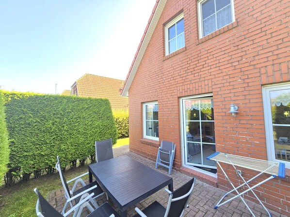 A brick house with a patio, a table, chairs, and a hedge.