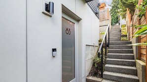 A modern building entrance with a glass door marked with the number 83, a small outdoor staircase, and a security camera. - Perch - Queen Anne 83 (Seattle)