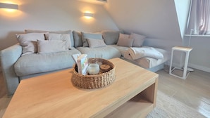 Una sala de estar moderna con un sofá seccional gris claro, una mesa de centro de madera con una cesta tejida y una mesita auxiliar blanca.