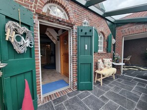 Ein Backsteinhaus mit grüner Tür, einer herzförmigen Dekoration und einem kleinen Tisch mit einem Stuhl davor.