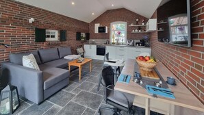 Espacio habitable compacto con sofá, mesa de comedor y área de cocina, destacando paredes de ladrillo y un techo inclinado.