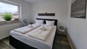 Ein Schlafzimmer mit Bett, Heizkörper, Fenster mit Pflanze, Wandregal und Gemälde.