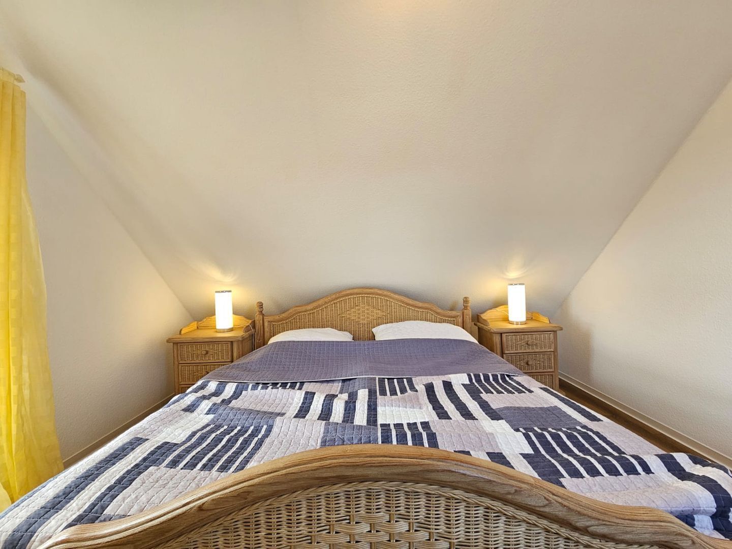 Ein Einzelbett mit gemustertem Bettbezug, zwei Nachttischlampen und einem Rattan-Kopfstück.
