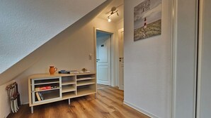 En smal hall med trägolv, en vit vägg och en hylla med böcker och en vas.
