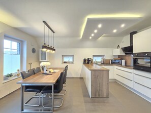 A modern kitchen with a central island, a dining area with a wooden table and chairs, and built-in appliances. - Ferienhaus Urlaubsglück - Herzlich Willkommen im "ferienhaus Urlaubsglück "! (Dornum)