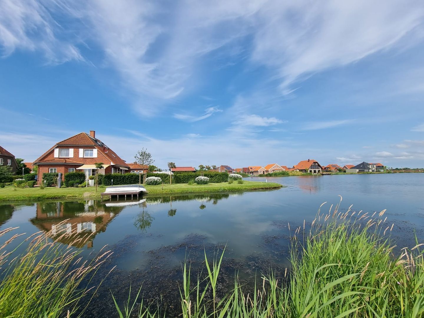Un quartier résidentiel paisible au bord d’un lac, avec des maisons, un quai et un ciel dégagé.