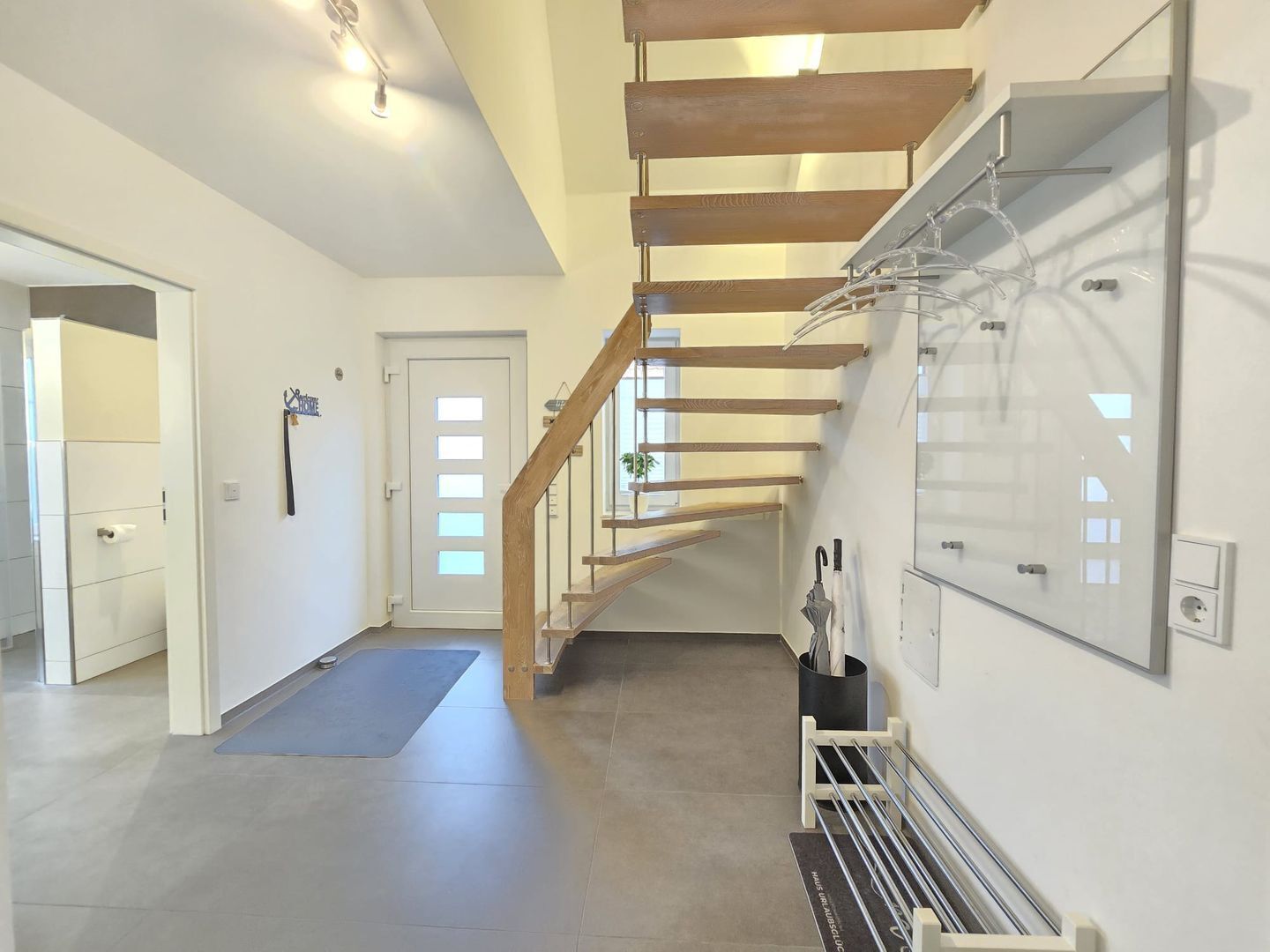 A modern interior with a wooden staircase, a hallway, and a wall-mounted drying rack.