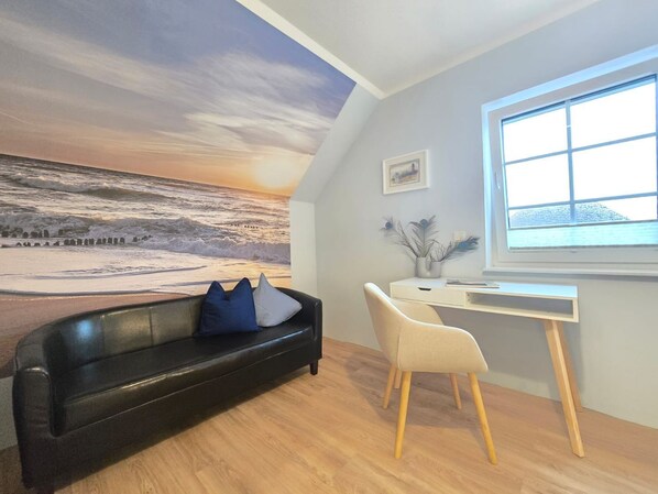 A room with a desk, a black leather couch, and a large mural of a beach scene.