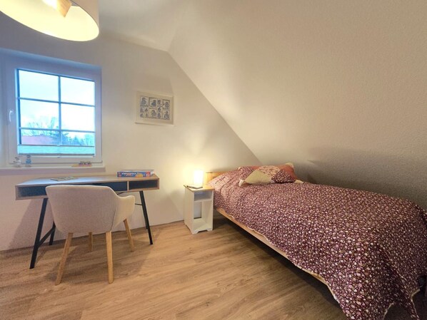 Una habitación pequeña y bien iluminada con escritorio, silla y cama.