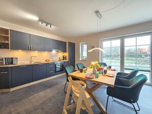 Une cuisine moderne avec des meubles de couleur sombre, un plan de travail en bois et un coin repas avec une table dressée pour quatre personnes.