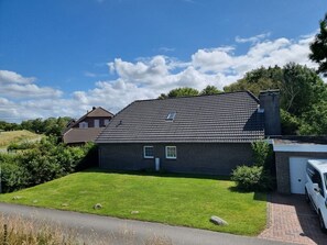 A modern two-story house with a dark roof and brick exterior, a well-maintained lawn, and a driveway leading to a garage.