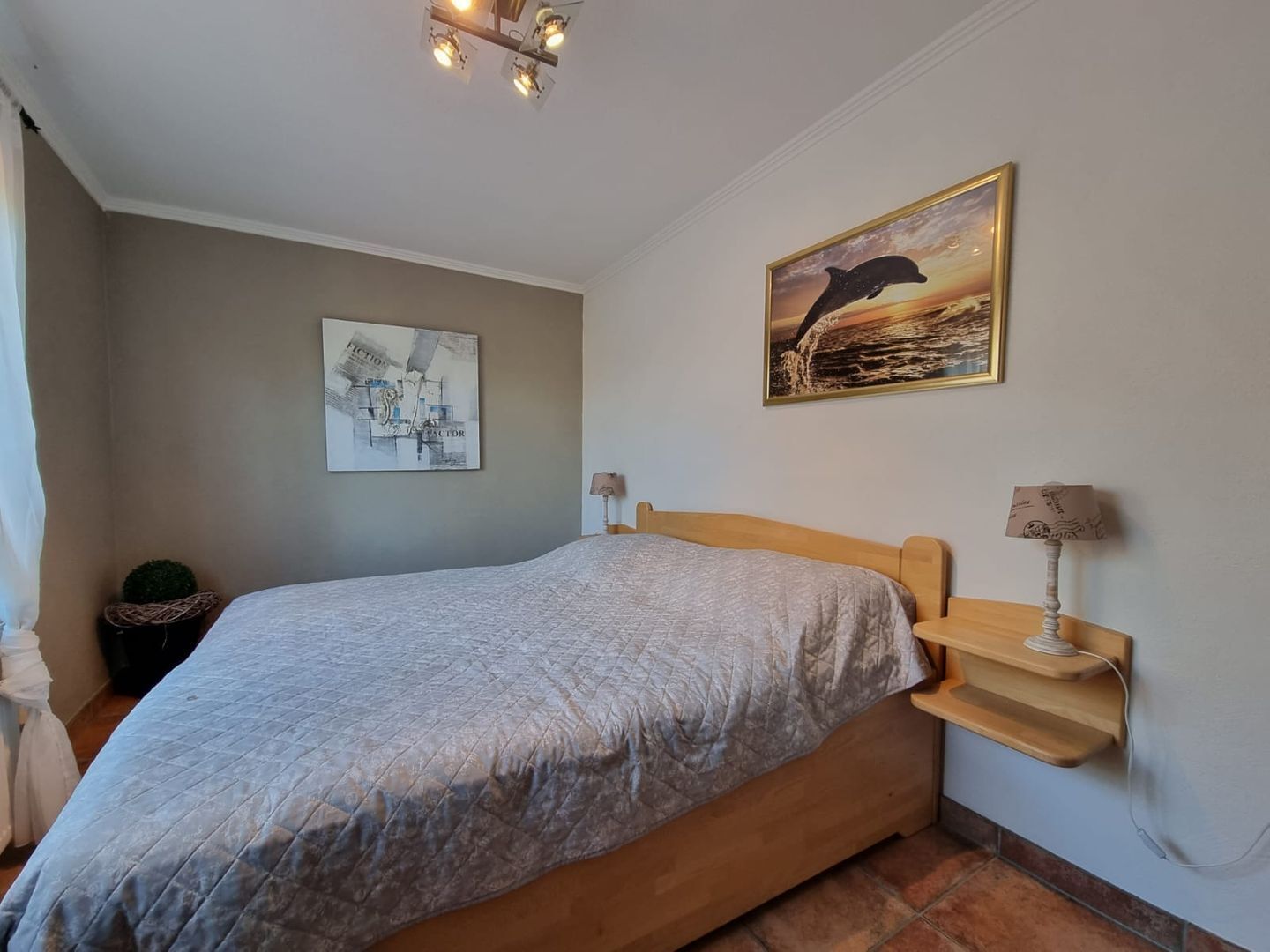 A bedroom with a bed, a nightstand, a lamp, a wall art of a dolphin, and a ceiling light fixture.