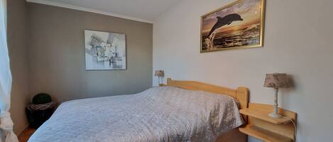 A bedroom with a bed, a nightstand, a lamp, a wall art of a dolphin, and a ceiling light fixture.
