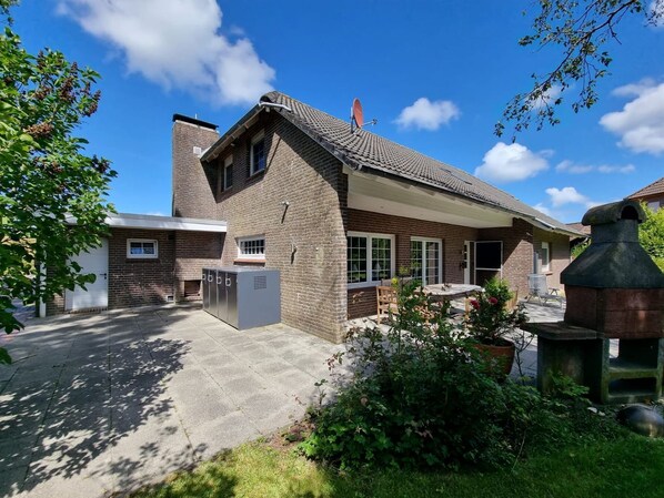 A two-story brick house with a tiled roof, a satellite dish, and a large outdoor grill.