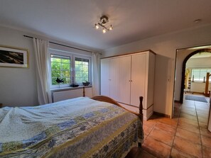 A bedroom with a bed, a window with curtains, a wardrobe, and a view of the outside.