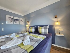 A bedroom with a bed, pillows, a bedside table, wall art, and a lamp. - Fewo Küstenquartier Dornumersiel - Hier Können Sie Entspannen. Die Neue Ferienwohnung Küstenquartier (Dornum)