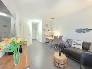 Uma sala de estar moderna com uma mesa de centro de madeira, um sofá cinza e um espaço de refeições com mesa e cadeiras.