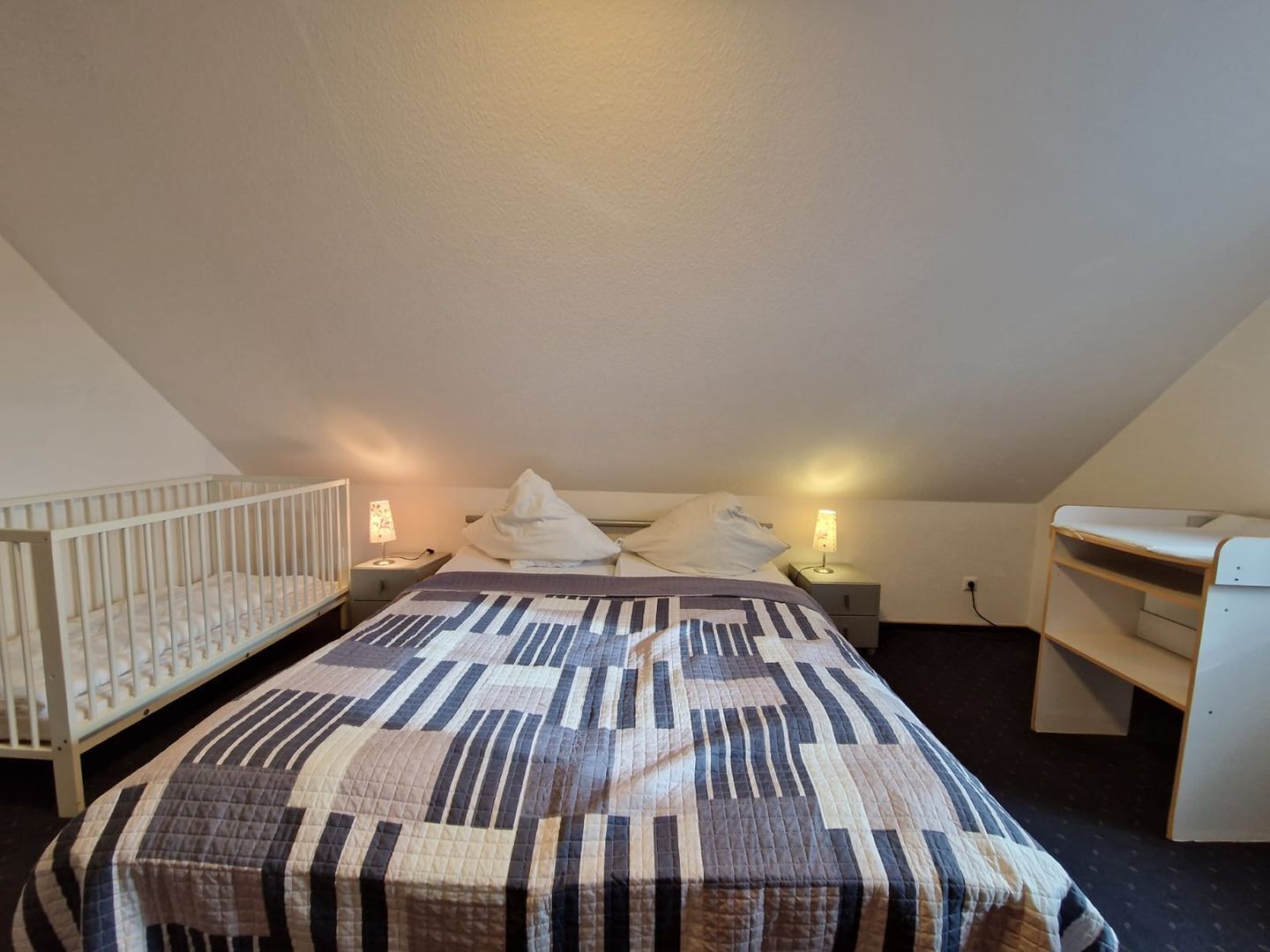 Un dormitorio con cama, cuna, mesita de noche y escritorio.