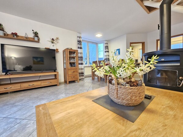 A modern living room with a TV, wooden entertainment unit, dining table, and a fireplace.