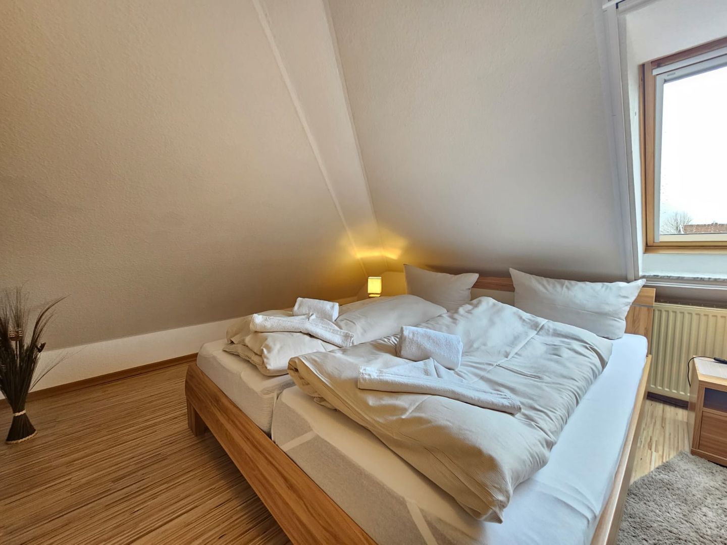 Ein Schlafzimmer mit Bett, Nachttisch, Lampe und Fenster.