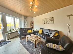 A modern living room with two black leather sofas, a wooden coffee table, and a bookshelf.