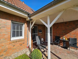 A brick house with a covered patio area featuring outdoor furniture and a small garden.