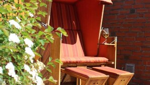 Un área de estar al aire libre con madera, un toldo a rayas, una pared de ladrillo y una copa de vino.