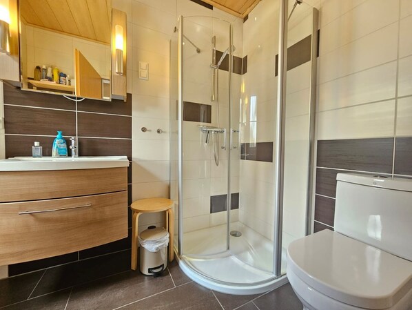 Un baño moderno con ducha envuelta en vidrio, tocador de madera con espejo y un inodoro.