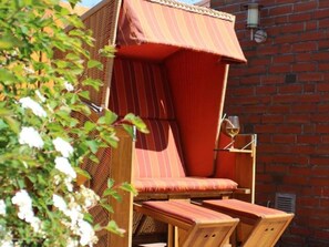 A wooden outdoor seating area with a striped canopy, a brick wall, and a glass of wine.