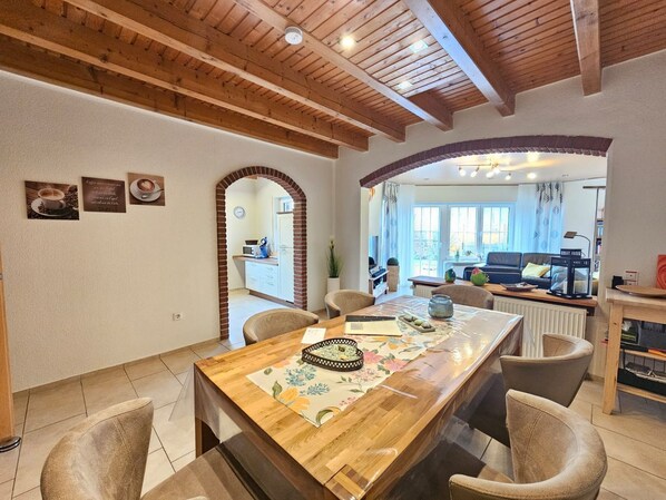 A dining area with a wooden table, chairs, and a kitchen visible through an archway.