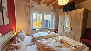 Un dormitorio con dos camas, techo de madera, ventana con cortinas, armario y televisión.