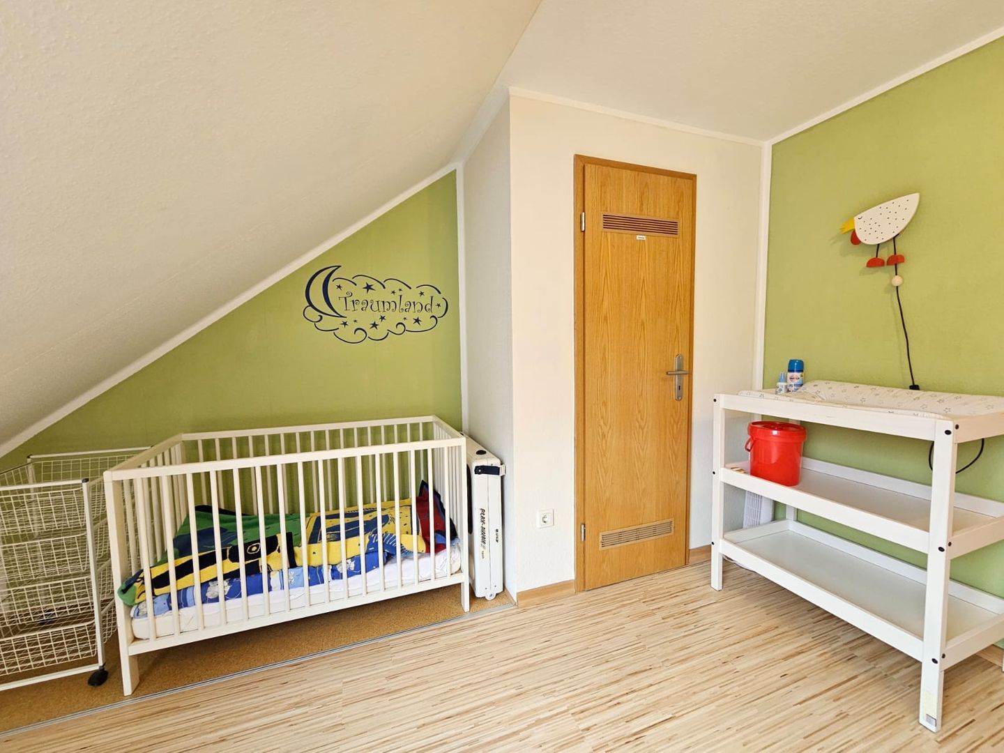 Une pièce avec un berceau, une porte en bois, un motif décoratif sur le mur et une étagère blanche.