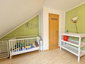Una habitación con una cuna, una puerta de madera, un adhesivo mural y un estante blanco.