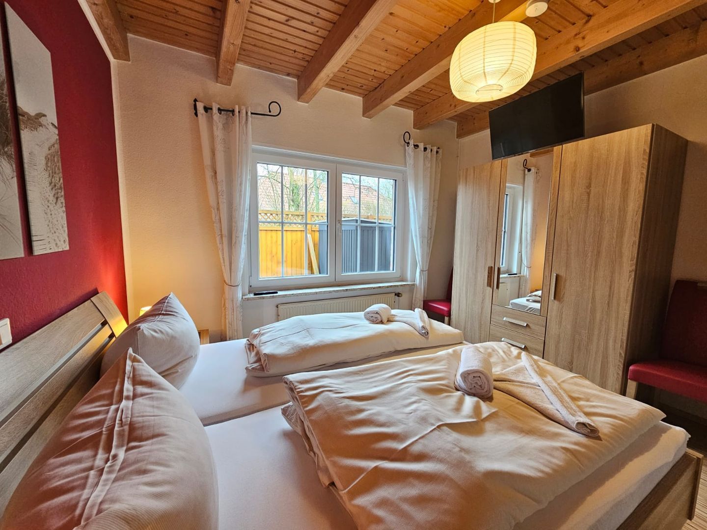 Une chambre avec deux lits, un plafond en bois, une fenêtre avec des rideaux, une armoire et un téléviseur.