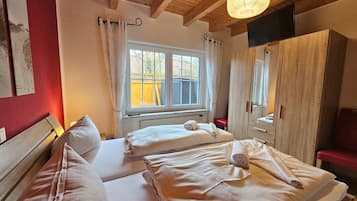 Une chambre avec deux lits, un plafond en bois, une fenêtre avec des rideaux, une armoire et un téléviseur.