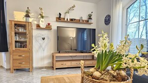 A living room with a TV, wooden cabinet, and a basket of flowers on a table.