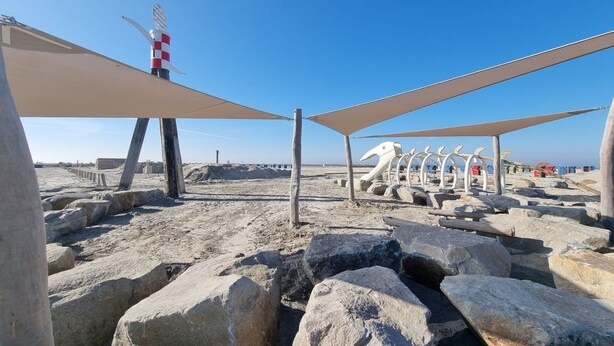 A beach with large rocks, a lifeguard tower, and beach umbrellas.