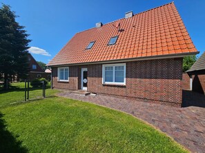 A two-story brick house with a red-tiled roof, a small front porch, and a well-maintained lawn.