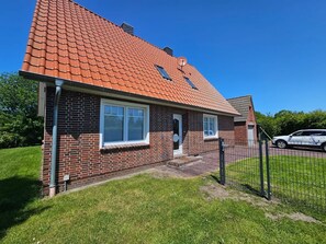 A single-story brick house with a red-tiled roof, a small front porch, and a fenced yard.