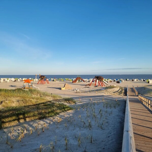 A beach with a wooden boardwalk, sand dunes, and beach huts.